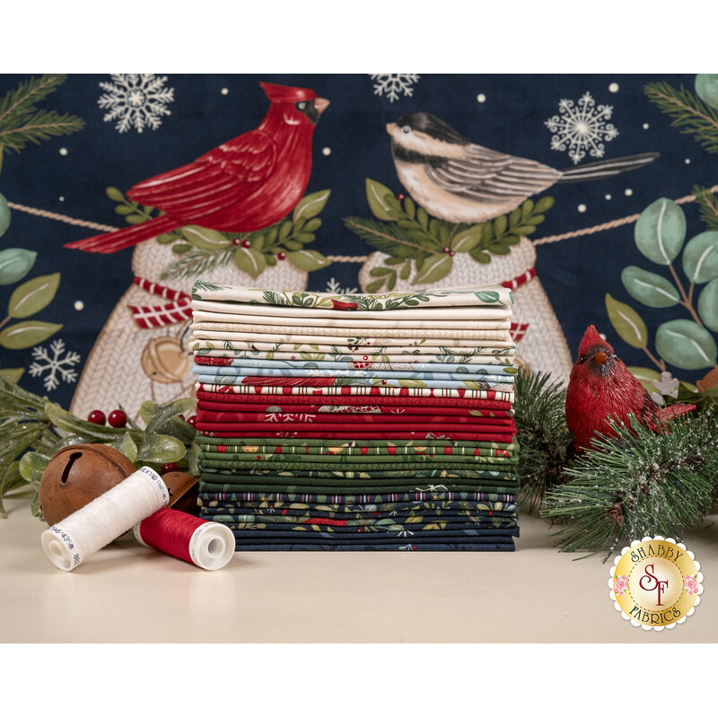 A stack of the fabrics included in the When Snow Falls F8 set, with a Panel in the background, and branches and mistletoe and a cardinal and a bell and thread.