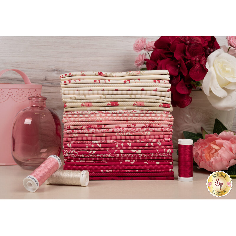 A stack of the fabrics included in the Petals and Polka Dots FQ set, with flowers and a vase and jars and thread.