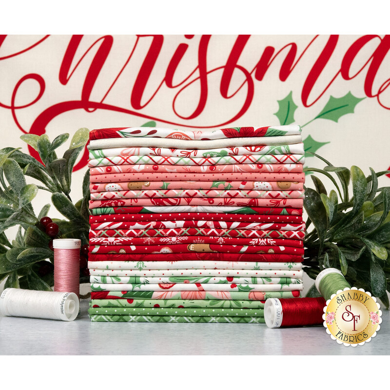 A stack of the fabrics included in the Merrily On High collection, with mistletoe and thread and the included panel.