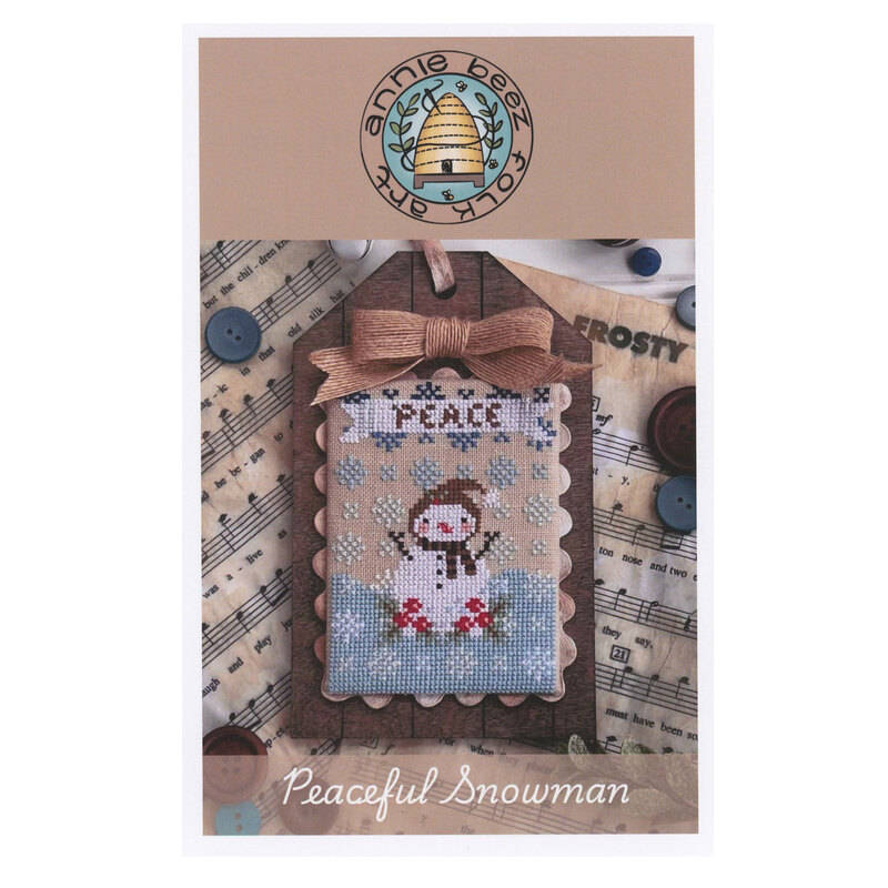 The front of the Peaceful Snowman Cross Stitch pattern by Annie Beez Folk Art showing the finished project mounted on a wood block. 