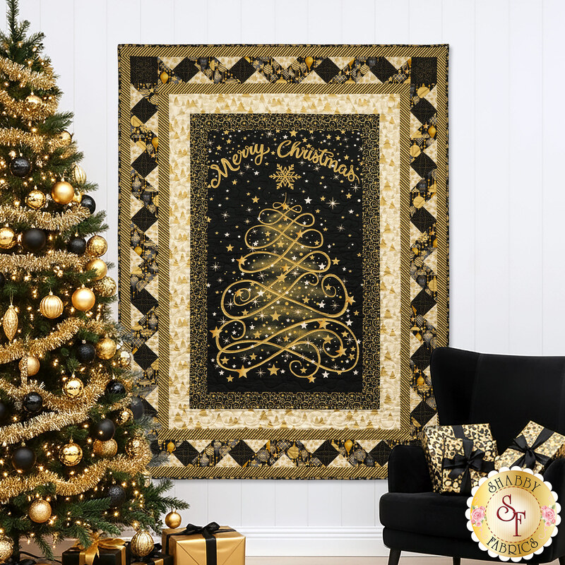 The completed Ribbon Border Panel Quilt colored in black, cream, and gold metallic fabrics from the Merry Christmas collection by Timeless Treasures, hung on a white paneled wall and staged with a modern black chair, decorated tree, and presents in coordinating colors.