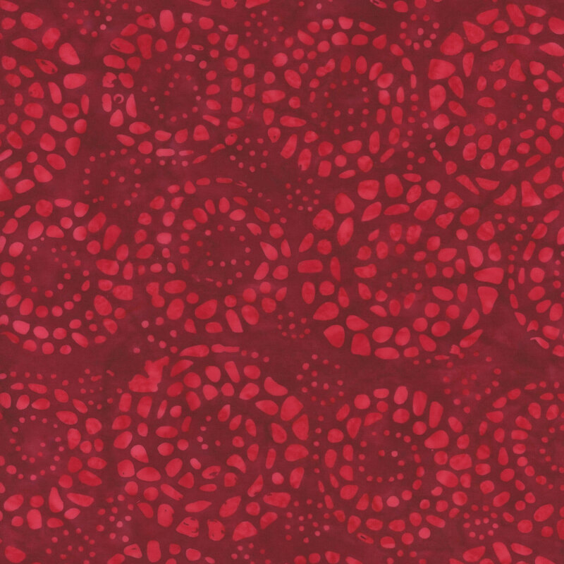 A tonal red batik fabric with dotted spirals.