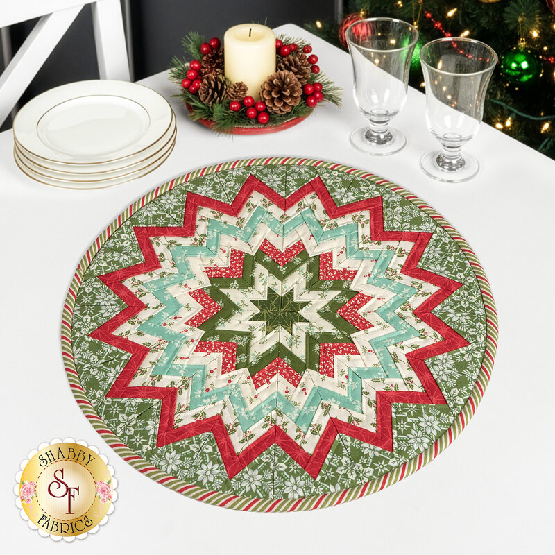 The completed Folded Star Table Topper colored in cream, teal, green, and red fabrics from the Sugarberry collection by Andover Fabrics, staged on a wood table with festive coordinating kitchen decor.