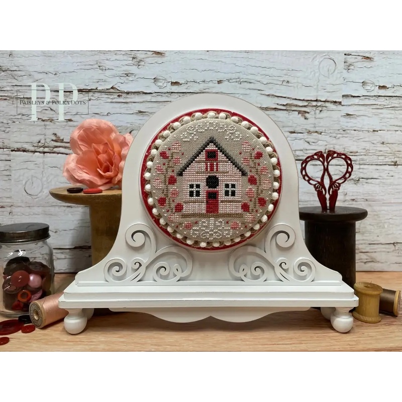 The fully assembled and painted Fleur Round Cross Stitch Frame, staged on a white tabletop next to sewing notions, displaying a festive cross-stitch project.