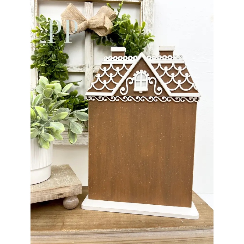 The fully assembled and painted All Seasons Gingerbread House Cross Stitch Display, staged on a wooden tabletop with complementary greenery and décor.