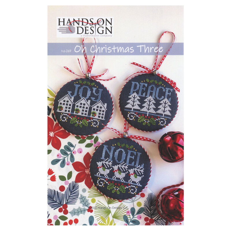 Front of pattern showing the completed cross stitch designs displayed on a white table with red Christmas bells.