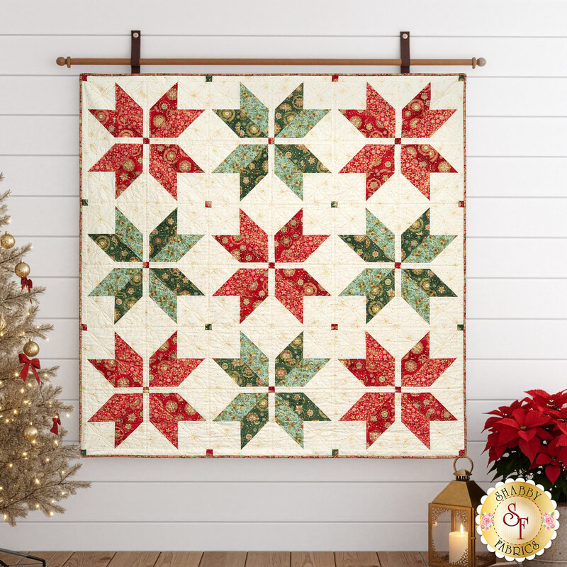 The completed Vintage Stars Quilt colored in Good Tidings fabrics, hung on a white paneled wall bordered by coordinating Christmas furniture and decor.