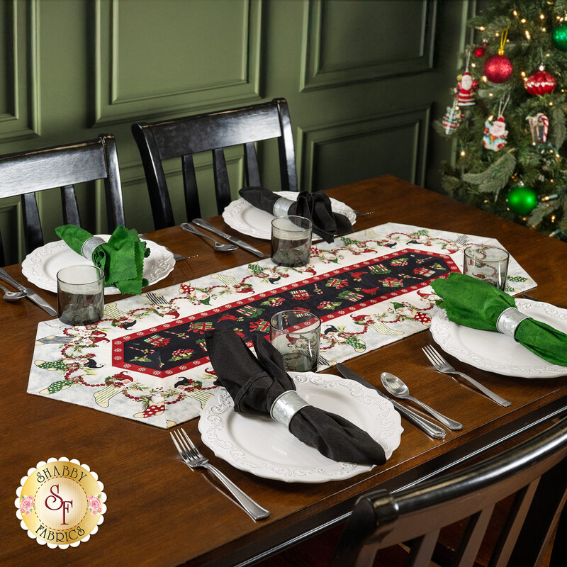 The completed Easy Striped Table Runner colored in red, white, and black fabrics from the Gnome-ments collection by Wilmington Prints, staged on a white table with four coordinating table settings.