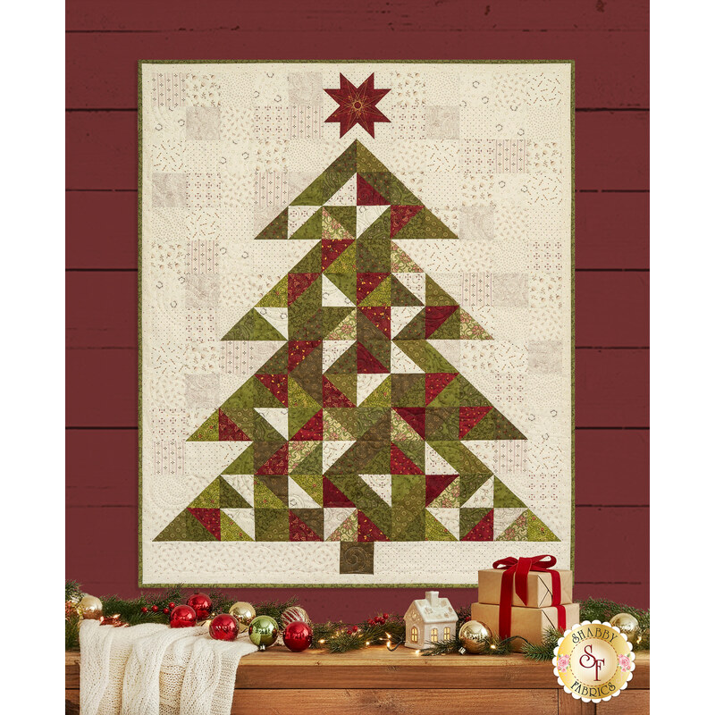 The completed Christmas Tree Quilt colored in red, cream, and green fabrics from the Baubles and Balsam collection by Henry Glass Fabrics, hung on a red wall and bordered by coordinating festive décor.