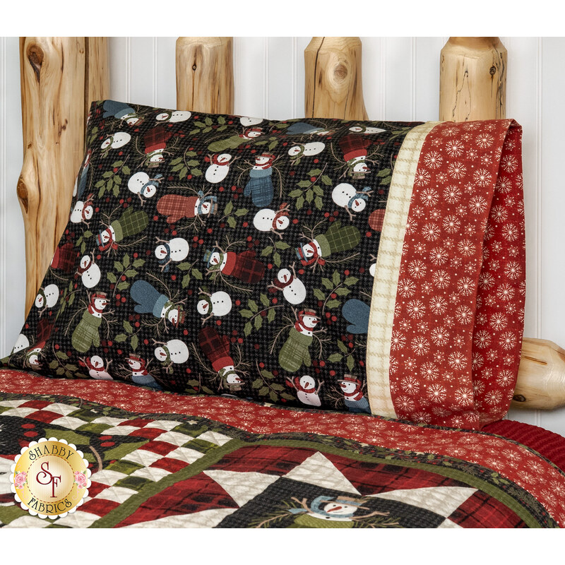 An angled shot of the Magic Pillowcase in black and red snowman fabrics from the Holly Jolly Flannel collection, staged on a bed with a matching patchwork quilt in a cabin setting.
