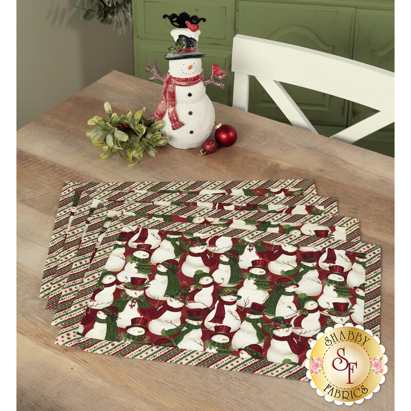 A shot of the four completed snowman-themed overlapping placemats in red, green, and cream fabrics, staged on a wooden table with coordinating napkins and décor.