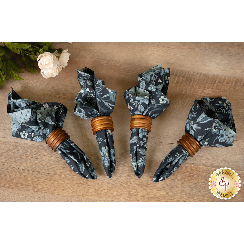 The completed napkins, colored in blue fabrics from the Sacre Blue collection by Moda Fabrics, staged on a wooden table with coordinating flowers.
