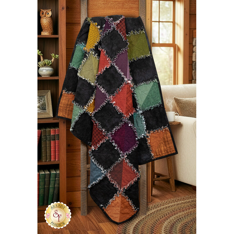The completed Half-Square Triangle Flannel Rag Quilt, colored in contrasting black and a rainbow of flannels in the Woolies Flannels collection, artfully draped from a wooden quilt ladder in a cozy cabin setting.