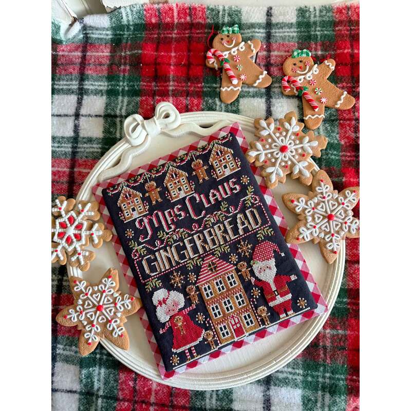 A festive plate with a cross stitched Mrs. Claus Gingerbread book surrounded by gingerbread cookies and snowflakes.