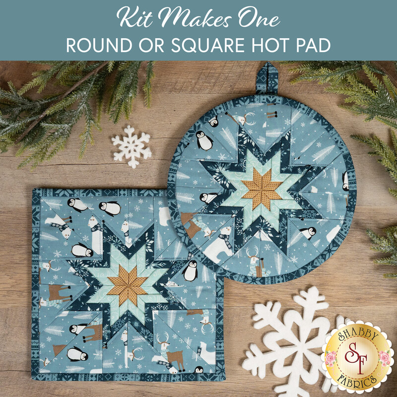 The two completed medium blue Folded Star Hot Pads, one round and one square, slightly overlapping each other and staged on a wooden table with coordinating winter décor.