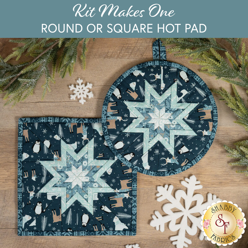 The two completed dark blue Folded Star Hot Pads, one round and one square, slightly overlapping each other and staged on a wooden table with coordinating winter décor.