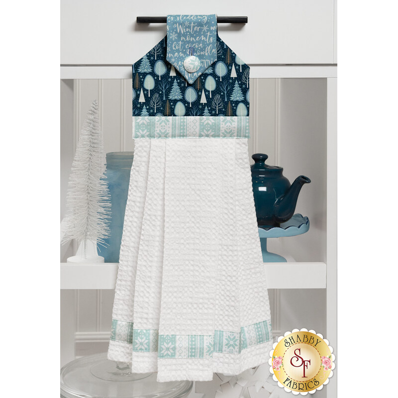 The Hanging Towel, colored in dark blue, teal and white fabrics from the Winter Magic collection, staged on a white kitchen drawer with coordinating decor.