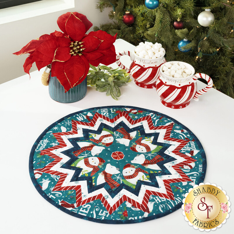 The completed Point of View Kaleidoscope Folded Star Table Topper colored in teal, white, and blue fabrics from the Woodland Wishes collection, staged on a white table with coordinating winter décor.