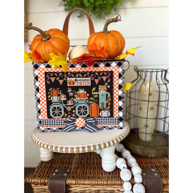A decorated basket with pumpkins and autumn leaves sits on a table, beside a lantern and beads.