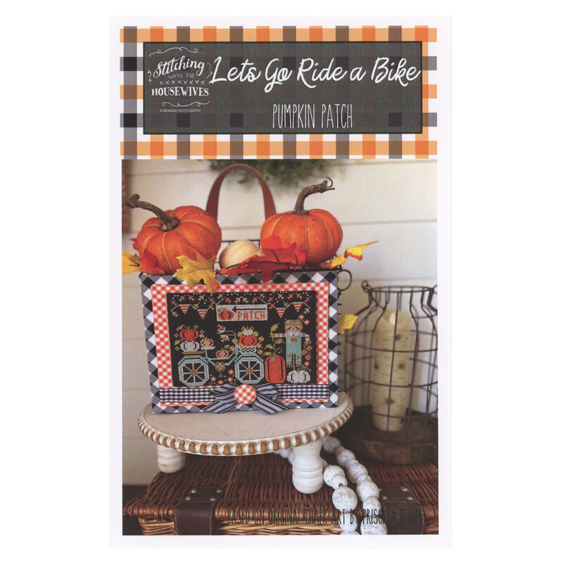 The front of the Lets Go Ride A Bike Pumpkin Patch cross stitch pattern showing the completed project featuring A blue bike in a fall scene surrounded by coordinating holiday décor. 