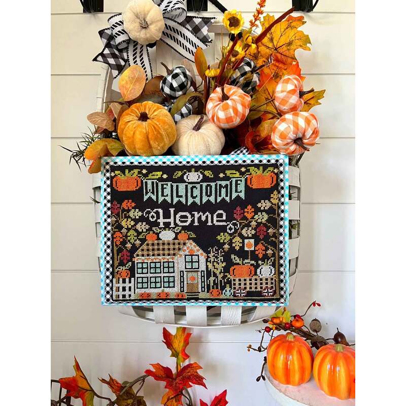 A decorative wall basket filled with fall items, featuring a cross stitched sign that reads “Welcome Home.”