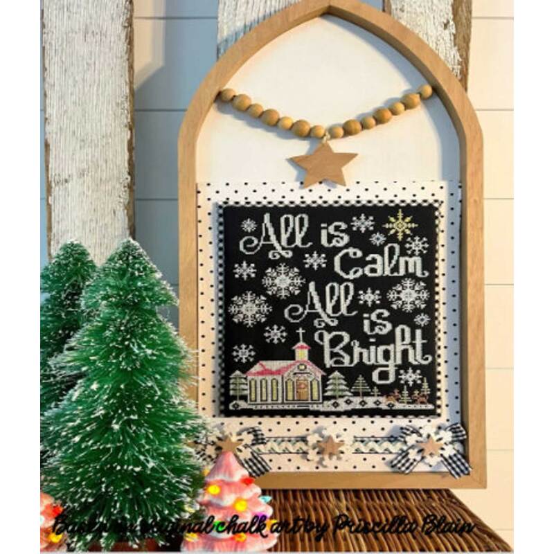Framed holiday cross stitch with All is Calm, All is Bright and a church illustration, surrounded by festive decor.