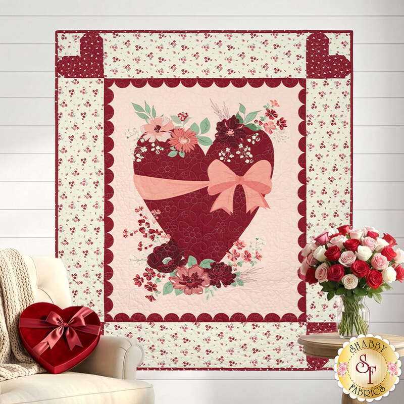 The completed Love You Always Heart Panel Quilt, colored in cream, pink, and red fabrics from the Love You Always collection by Riley Blake Designs, hung on a white shiplap wall and staged with coordinating furniture and décor.