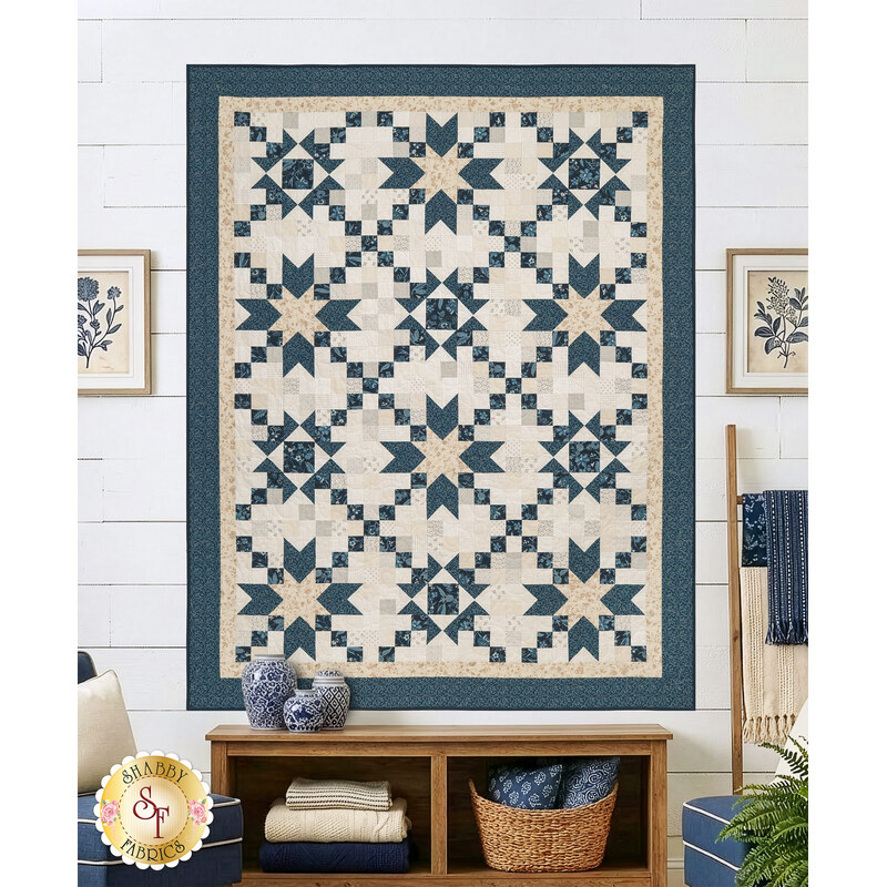 The completed Chain of Stars quilt, colored in blue fabrics from the Sacre Bleu collection and cream fabrics from the Itty Bitty Backgrounds collection, staged on a white shiplap wall and staged with coordinating furniture and décor.