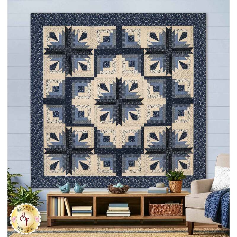 The completed Cactus In The Cabin quilt, colored in rich cream, denim blue, and navy blue fabrics from the Bluebird's Nest collection by Moda Fabrics, staged on a blue shiplap wall in a cozy, modern living room with coordinating décor.