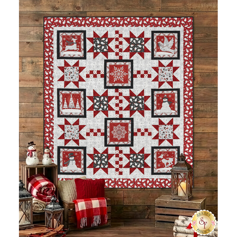The completed Blizzard Fun Quilt, colored in gray, red, and black fabrics from the Blizzard Fun collection by Henry Glass Fabrics, staged on a rustic wood cabin wall with coordinating pillows and décor.