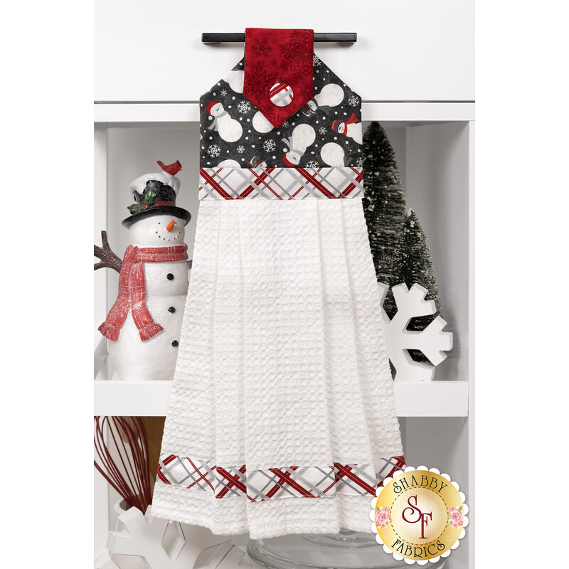 The completed Hanging Towel, colored in black, red, and white fabrics from the Blizzard Fun collection by Henry Glass Fabrics, hung on a kitchen drawer and staged with coordinating winter and kitchen décor.