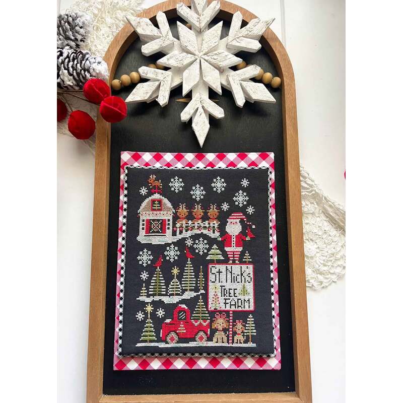 A festive cross stitched winter-themed decoration featuring a stitched scene of St. Nick's tree farm, snowflakes, and a red truck.