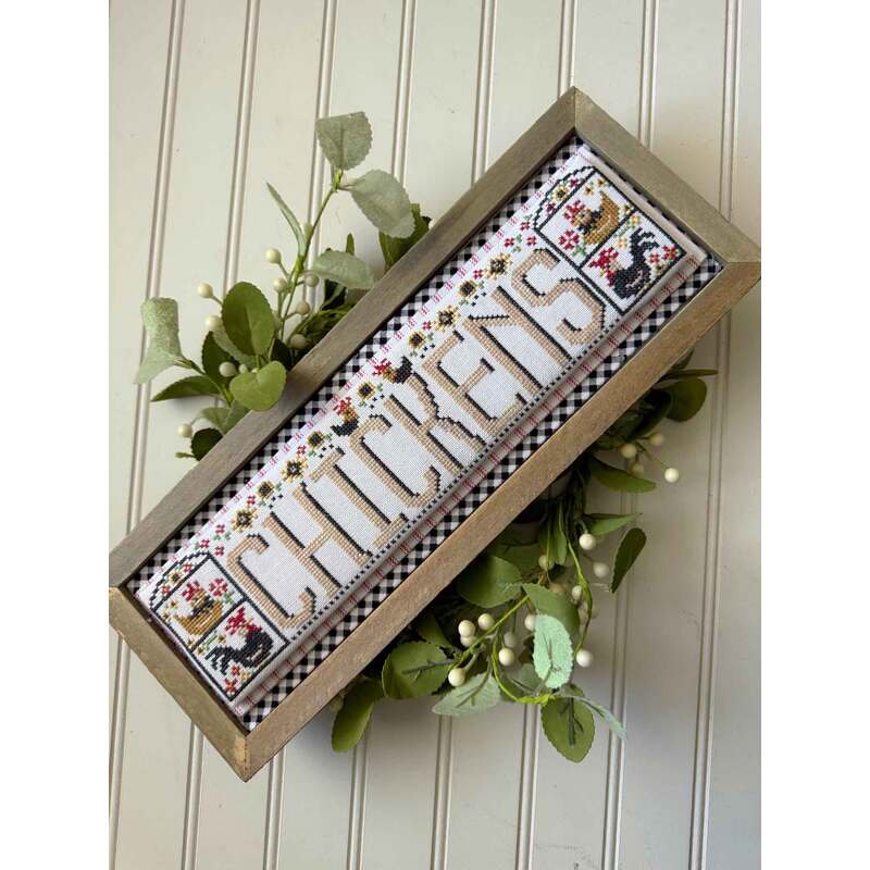 The front of the Chickens Word Swap cross stitch pattern showing the completed project surrounded by coordinating holiday décor. 
