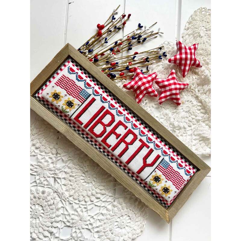 Decorative frame featuring a cross stitched word LIBERTY, accented by fabric stars and floral patterns.