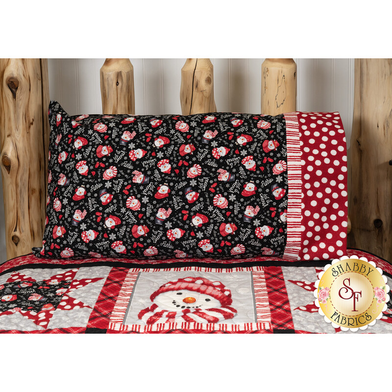 The Snow Crew Flannel pillowcase, colored in fabrics featuring snowmen wearing red hats in white, red and black prints. The pillowcase is staged on a bed with the coordinating Snow Crew Besties Quilt.