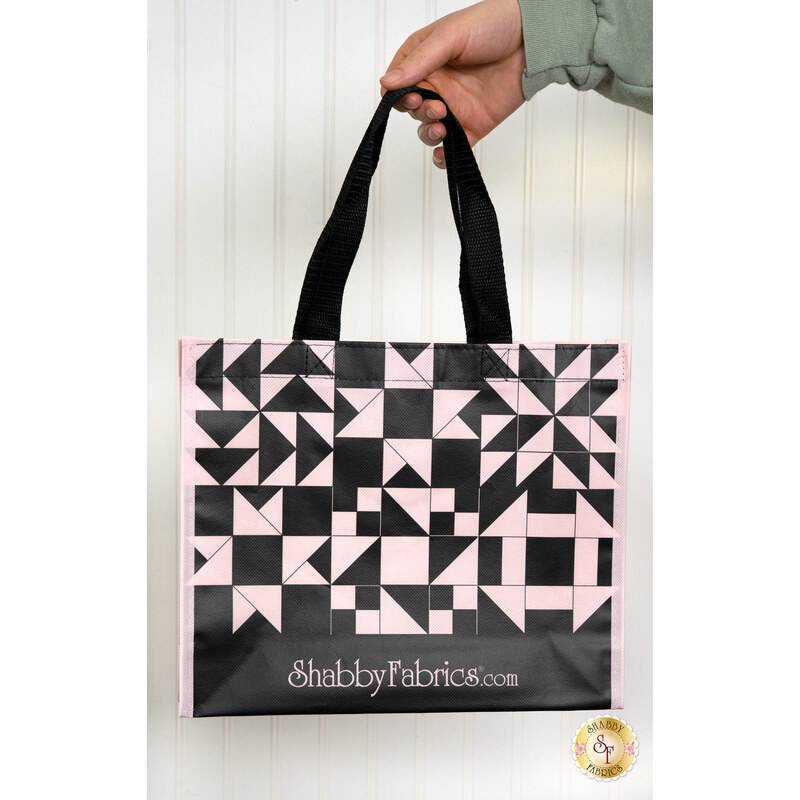 A model holds the medium sized Shabby Fabrics Tote Bag in front of a white paneled wall.