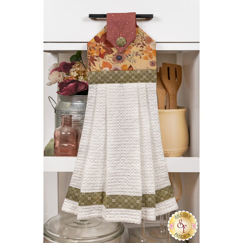 The Hanging Towel, colored in yellow, burnt orange and green fabrics from the Evening On The Prairie collection, staged on a white kitchen drawer with coordinating decor.