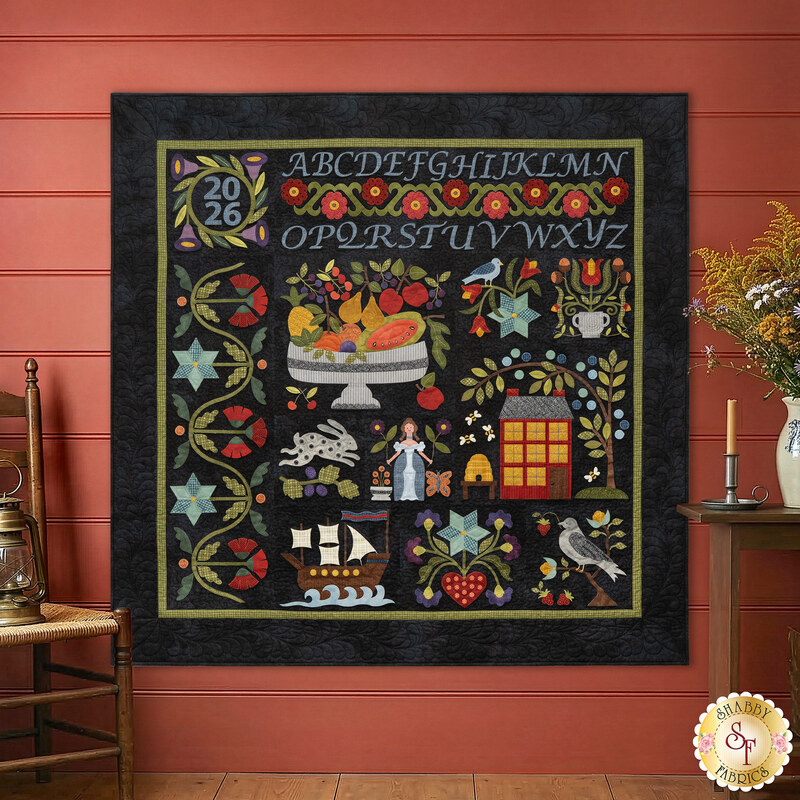 The completed Samplemaker quilt, colored in vibrant fabrics from the Woolies Flannel collection by Maywood Studio, staged on a red paneled wall with coordinating décor.