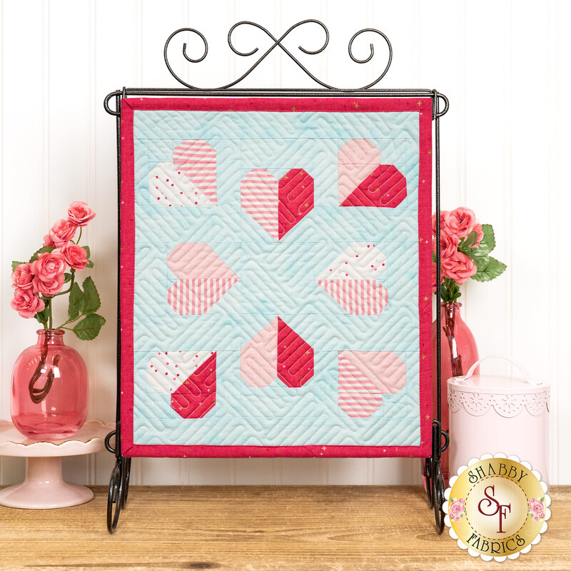 The completed Tender Heart Tabletop Banner, a series of pink and white patchwork hearts on a blue mottled fabric, staged with coordinating décor.