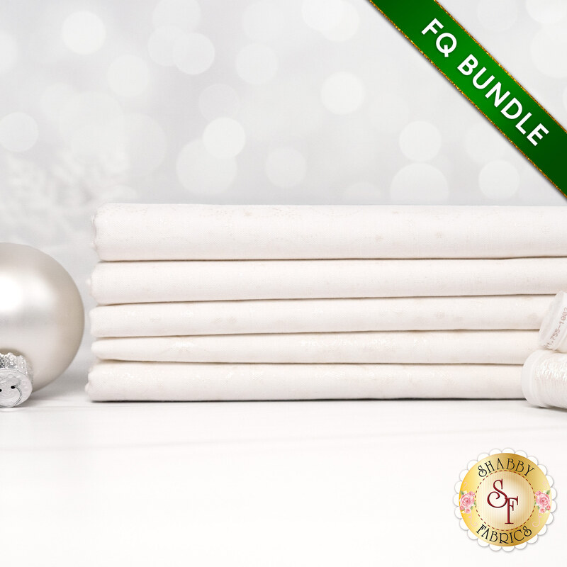A stack of the five fabrics included in the 5 FQ Bundle White/Pearl by Stof Fabrics, with thread and a snowflake.