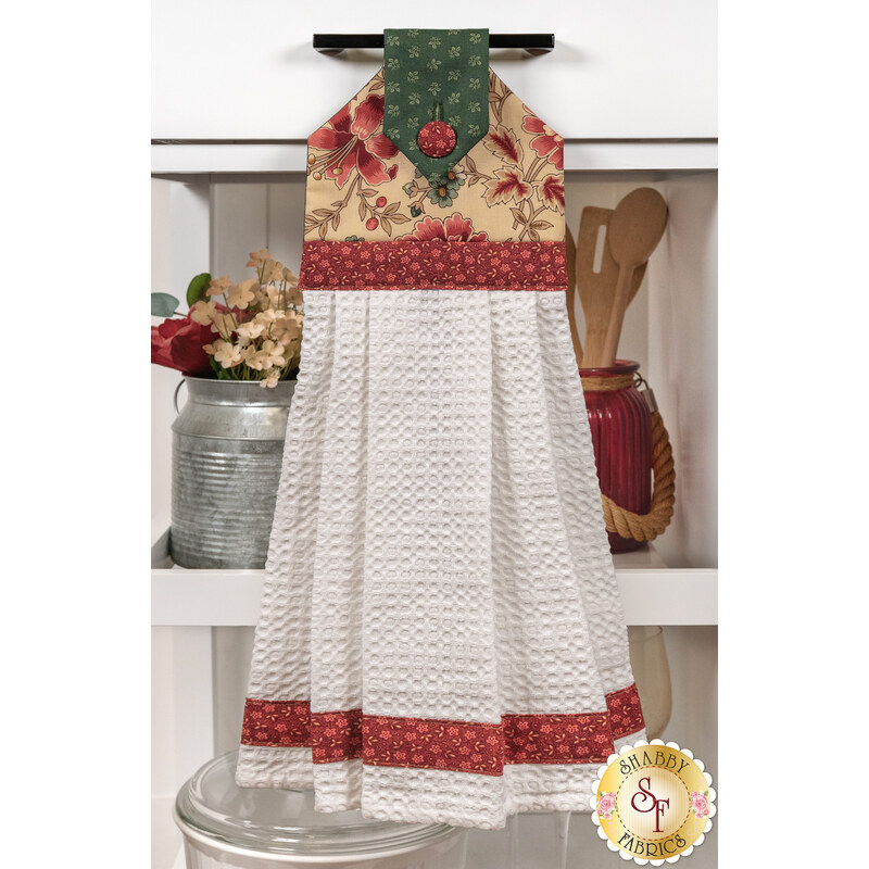 A head on shot of the completed brown Hanging Towel, colored in tan, pink, and green fabrics from the Always and Forever collection by Andover Fabrics, hung on kitchen drawer and staged with coordinating décor.