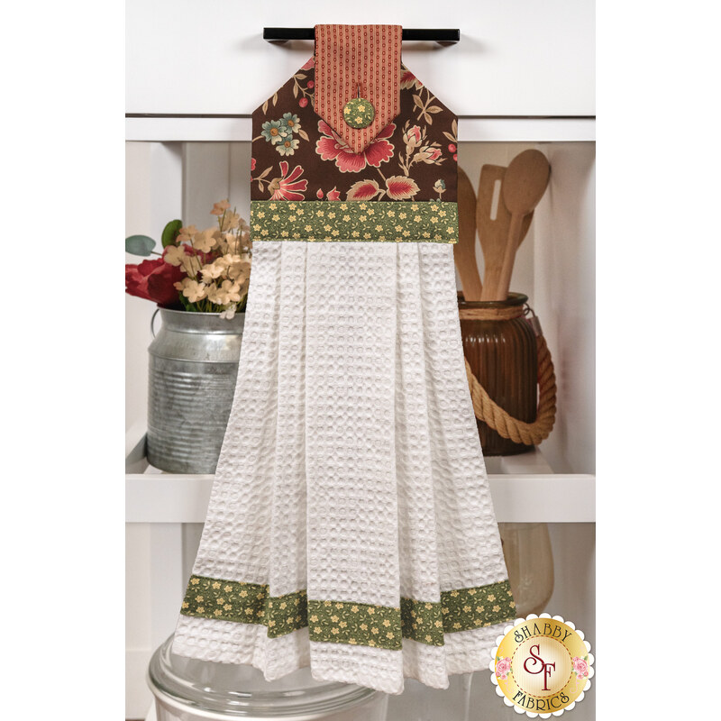 A head on shot of the completed brown Hanging Towel, colored in brown, pink, and green fabrics from the Always and Forever collection by Andover Fabrics, hung on kitchen drawer and staged with coordinating décor.