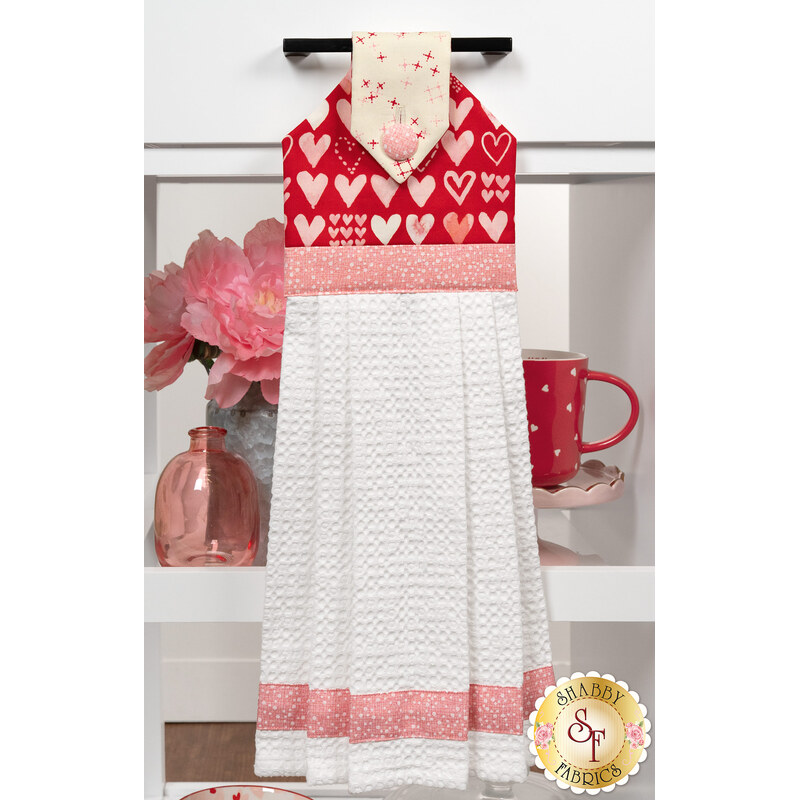 A head on shot of the completed red Hanging Towel, colored in bold pink, red, and cream fabrics from the Darling Peony collection by Moda Fabrics, hung on kitchen drawer and staged with coordinating décor.