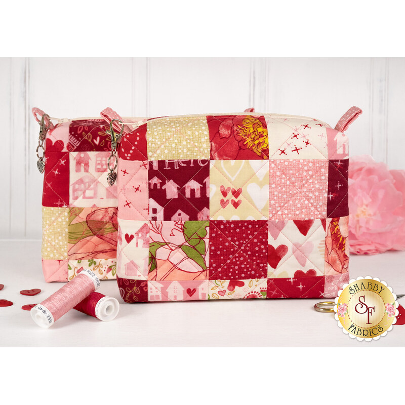 The two completed Mini-Charm bags, colored in bold pink, red, and cream fabrics from the Darling Peony collection by Moda Fabrics, staged on a white countertop with coordinating décor. 