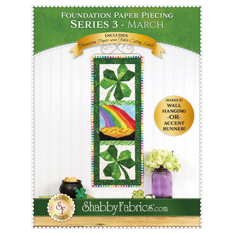 Front cover of the pattern, showing the completed project featuring two bright green shamrocks framing a pot of gold at the end of a rainbow, hung on a white wall and staged with coordinating décor.
