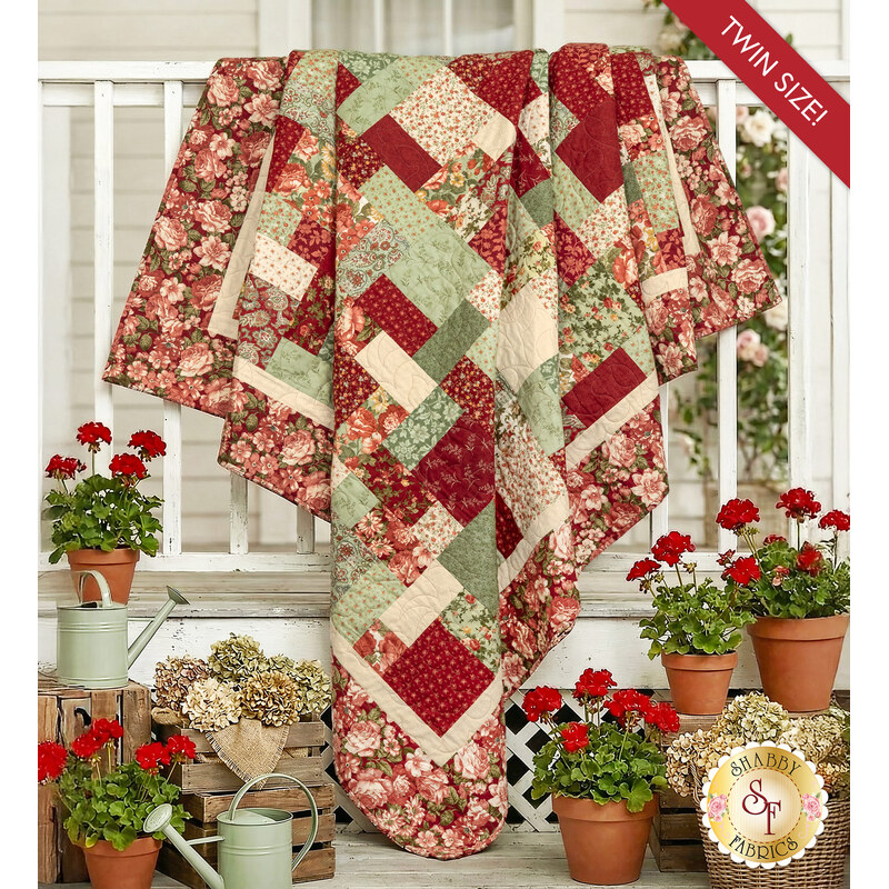 The completed Easy as ABC and 123 quilt kit - Ambiance, draped over a white porch surrounded by red geraniums. 