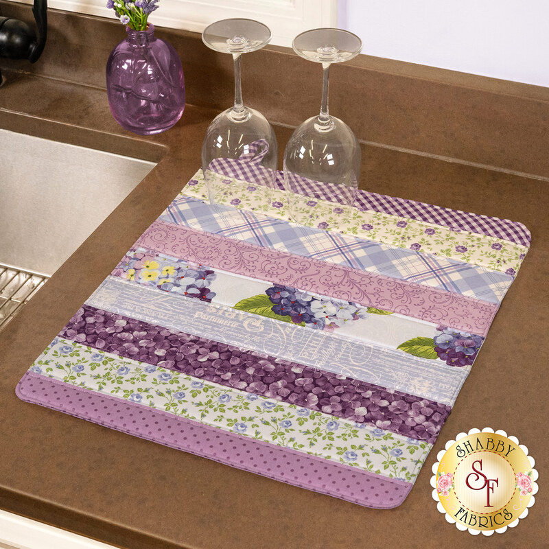 The completed Dry Ideas drying mat, colored in periwinkle blue florals fabrics from the Hydrangeas in the Garden collection by Riley Blake Designs. The project is staged on a kitchen counter with coordinating decor.