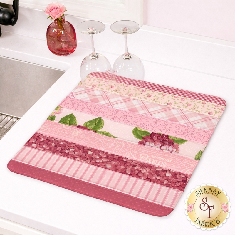 Pink patterned kitchen drying mat with stripes of floral and geometric designs, placed next to wine glasses.