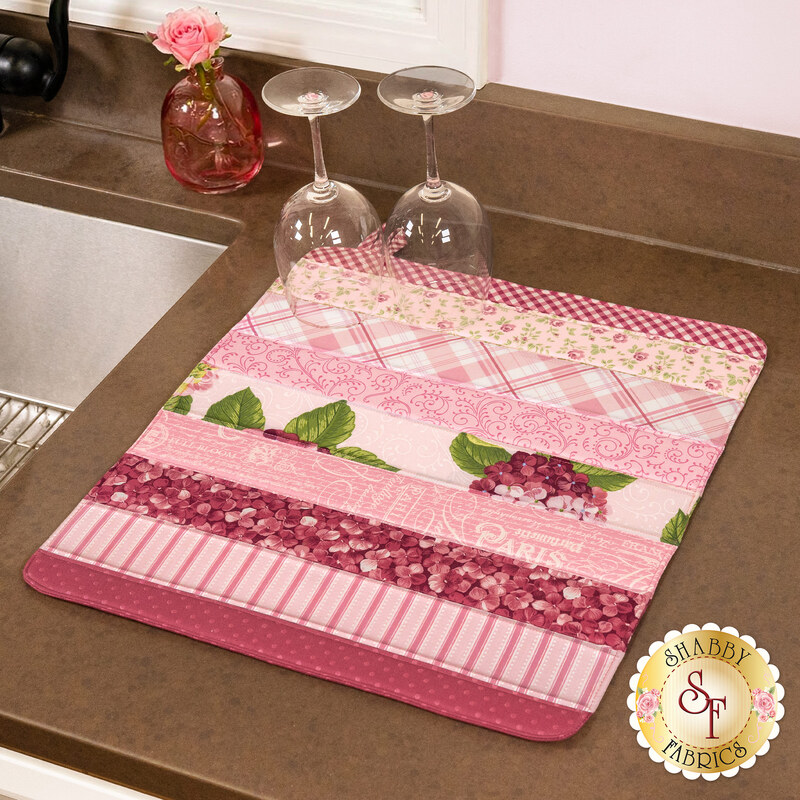 The completed Dry Ideas drying mat, colored in pink florals fabrics from the Hydrangeas in the Garden collection by Riley Blake Designs. The project is staged on a kitchen counter with coordinating decor.