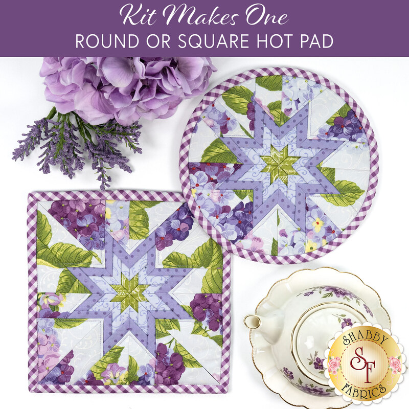 The two completed Folded Star Hot Pads, colored in periwinkle blue florals fabrics from the Hydrangeas in the Garden collection by Riley Blake Designs, staged on a white table with coordinating floral décor and a teapot.